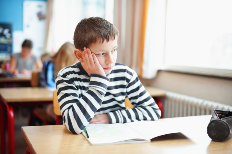 Ein Schuljunge sitzt in der Schule am Tisch und schaut gelangweilt aus dem Fenster