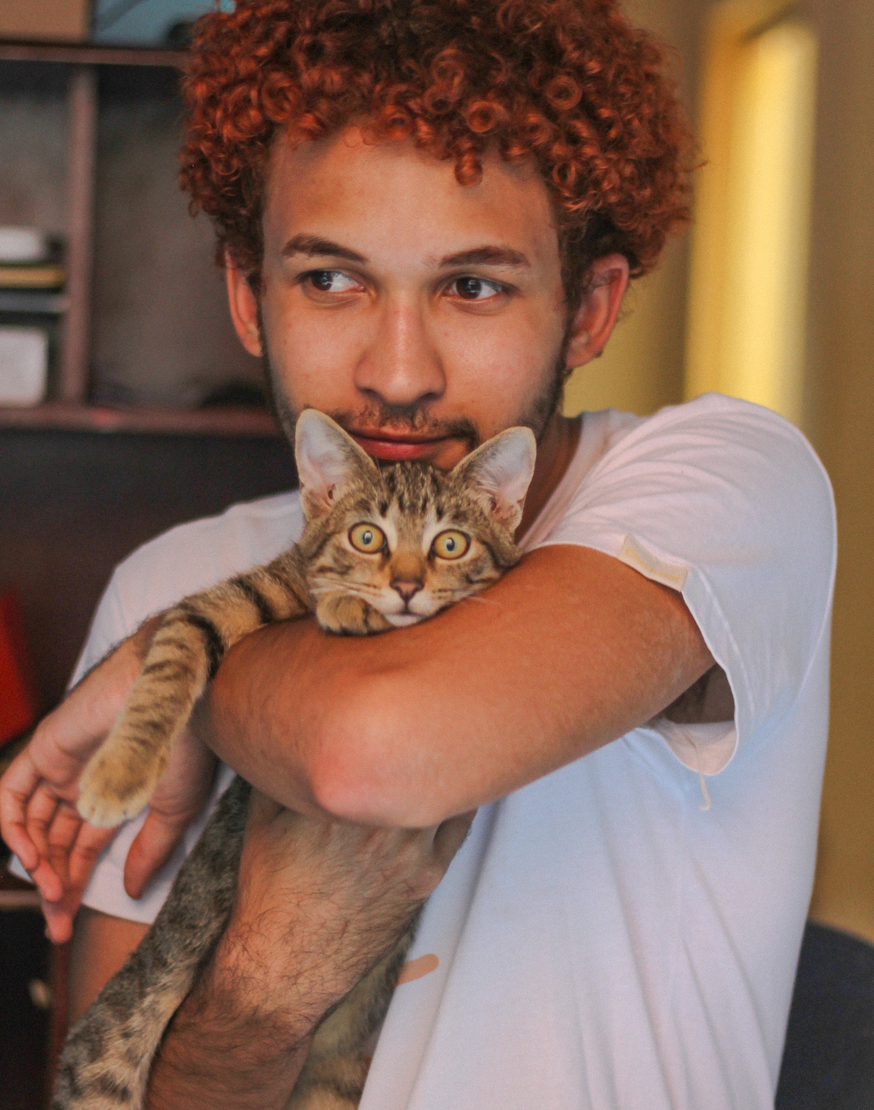 Ein Mann mit weißem T-Shirt hält seine Katze im Arm.