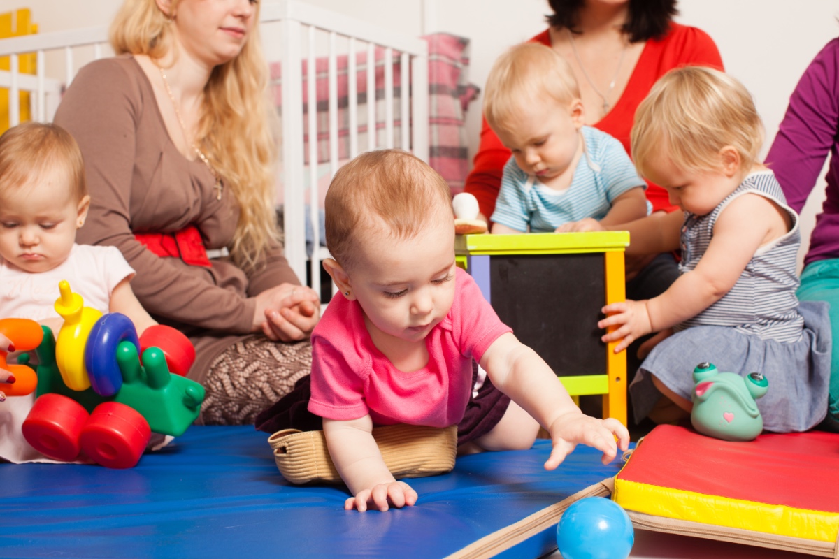 Eine Gruppe Kleinkinder werden in einer Kita von Erzieherinnen betreut.