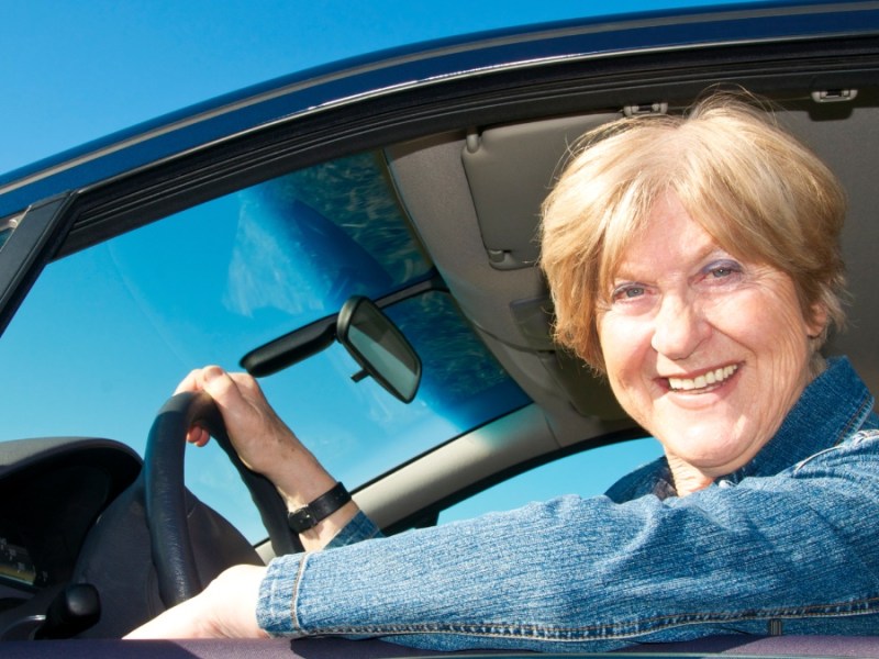 Eine lächelnde ältere Frau sitzt in einem Auto.