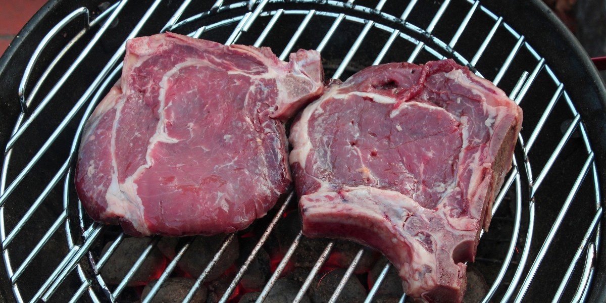 Zwei rohe Steaks liegen auf einem Grill.