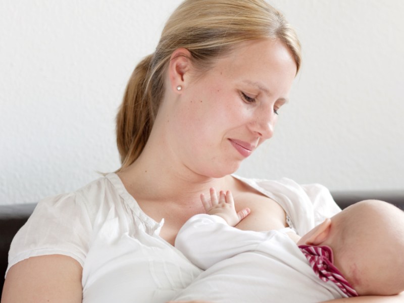 Eine Mutter sitzt auf einem Sofa und stillt ihr Baby.