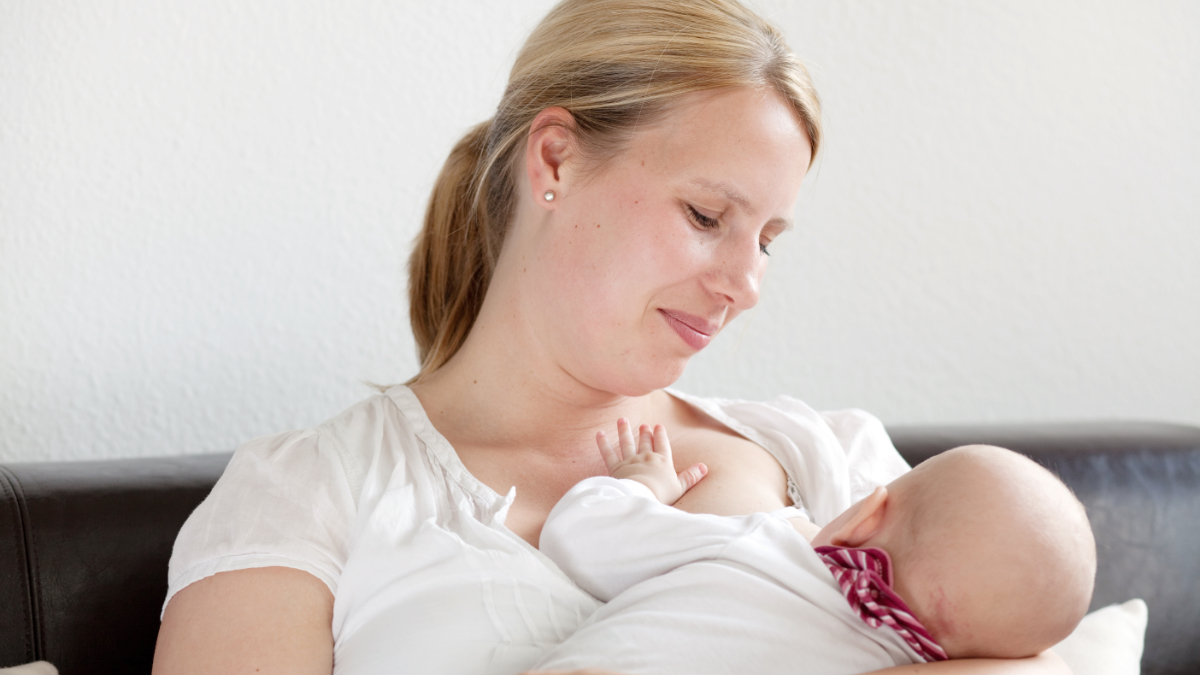 Eine Mutter sitzt auf einem Sofa und stillt ihr Baby.