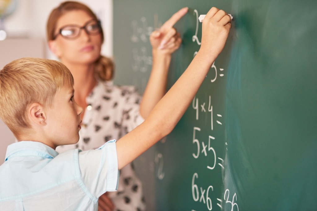 Matheunterricht: Schüler steht an der Tafel, die Lehrerin daneben.