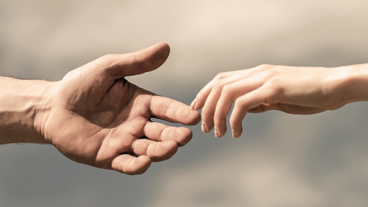 Die Hand eines Mannes greift nach der Hand einer Frau vor einem blauen Himmel.