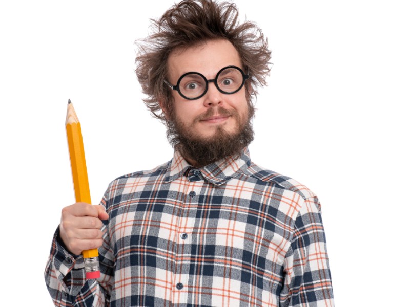 Ein verrückter, bärtiger Mann mit Brille und riesigem Bleistift in der Hand vor weißem Hintergrund.