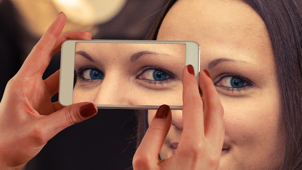 Eine optische Täuschung von einer Frau, die sich ihr Smartphone wie eine Maske vor das Gesicht hält.