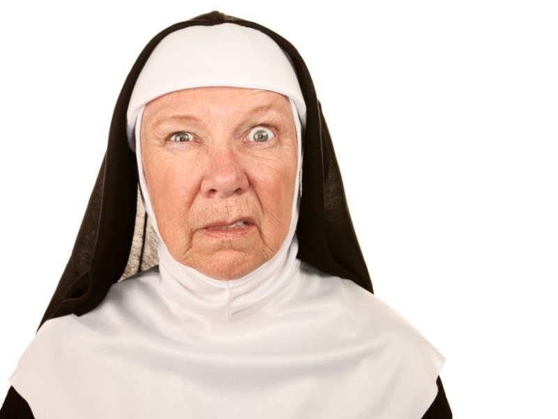 Eine ältere Nonne, die eine witzige Grimasse zieht, vor einem weißen Hintergrund