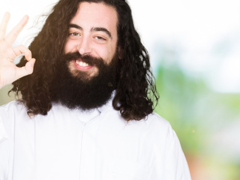 Ein Mann trägt ein Jesus-Kostüm und macht ein OK-Zeichen mit seiner rechten Hand.